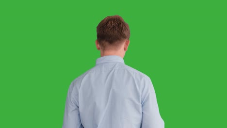초록색 스크린 앞에서 연기하는 젊은 잘생긴 남성, 금발, 파란 셔츠, 파란 바지, 춤추고, 생각하고, 돌아서서 카메라와 대화합니다.