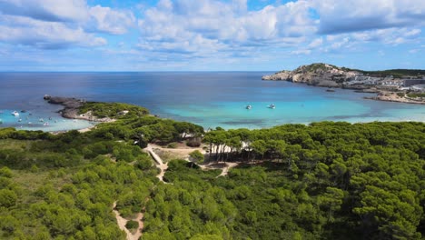 witness the stunning landscape of cala agulla in cala rajada, mallorca, featuring clear blue waters, lush greenery, and boats sailing along the coastline. a perfect spot for relaxation and adventure.