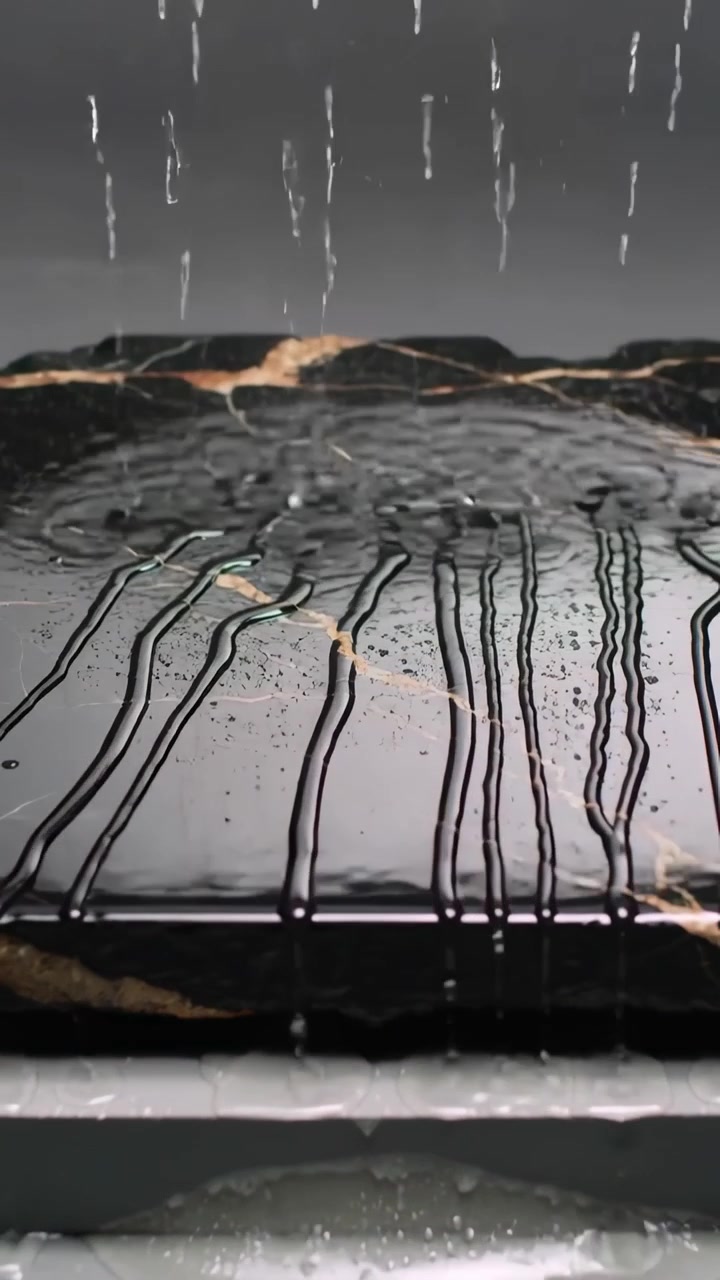 Vertical video: Increasing droplets, striking black marble slab at tabletop, tracing gold vein