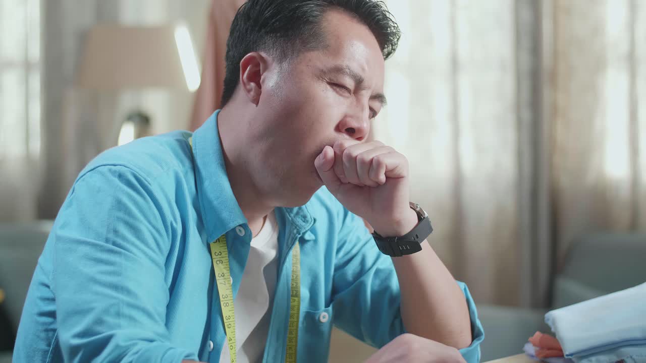 Close Up Of Asian Male Designer Working On A Laptop, Yawning, And Sleeping While Designing Clothes In The Studio