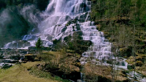 beautiful waterfall along mountain slope surrounded by tree forest on a bright sunny day