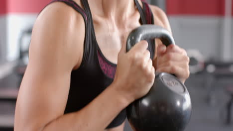 blurred gym background frames a young caucasian woman with kettlebells, with copy space