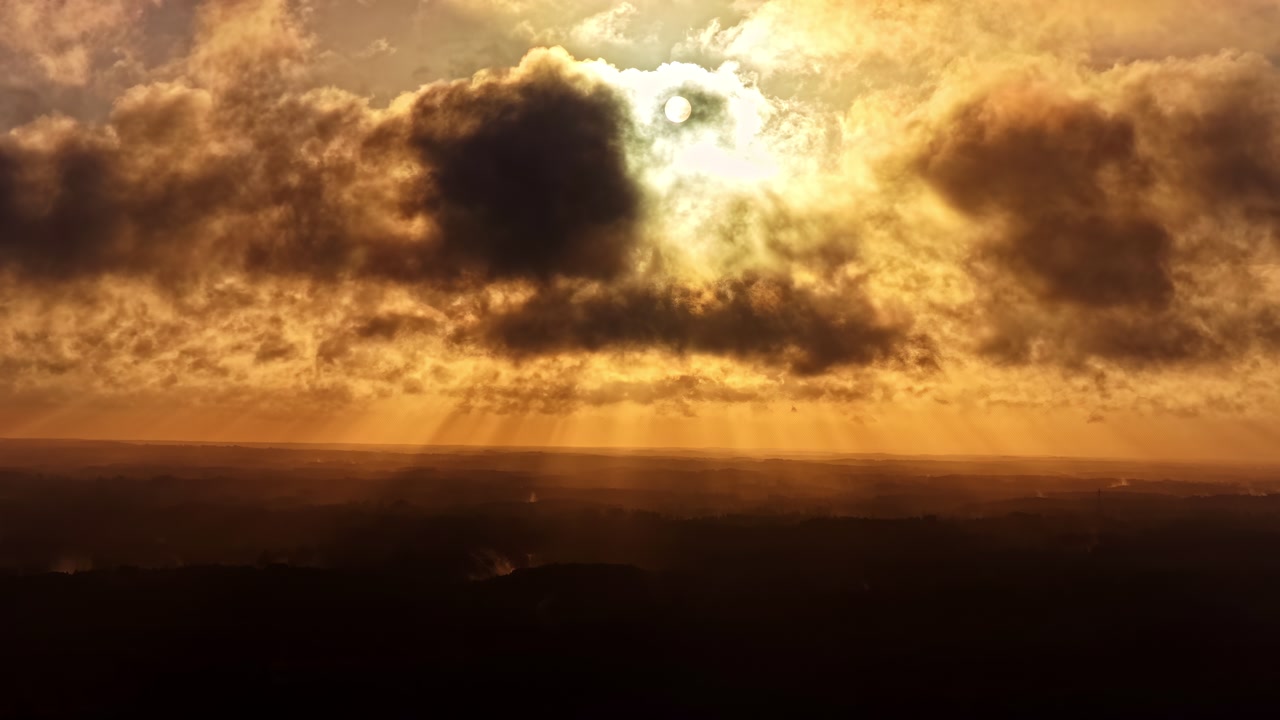 Aerial view of golden sun rays piercing through dark clouds at sunsets