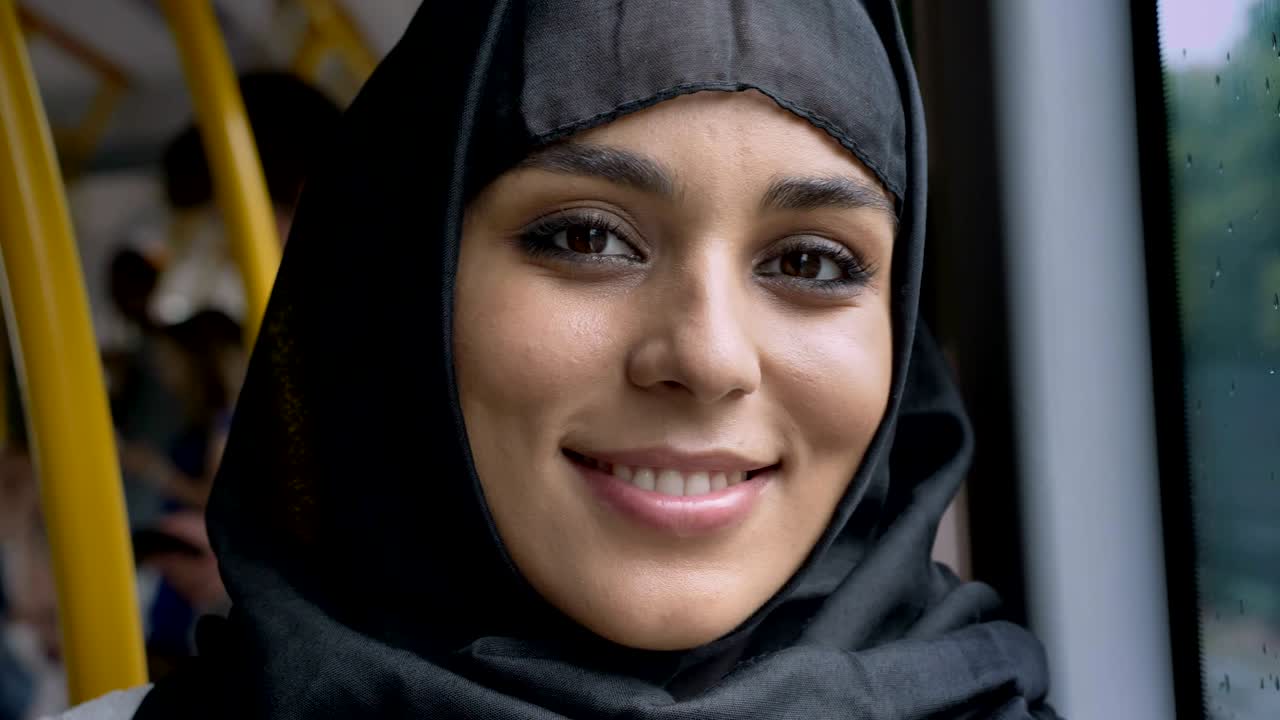 Young sweet muslim woman in hijab is watching at camera in bus, transport concept, urban concept, weather concept, dreaming concept
