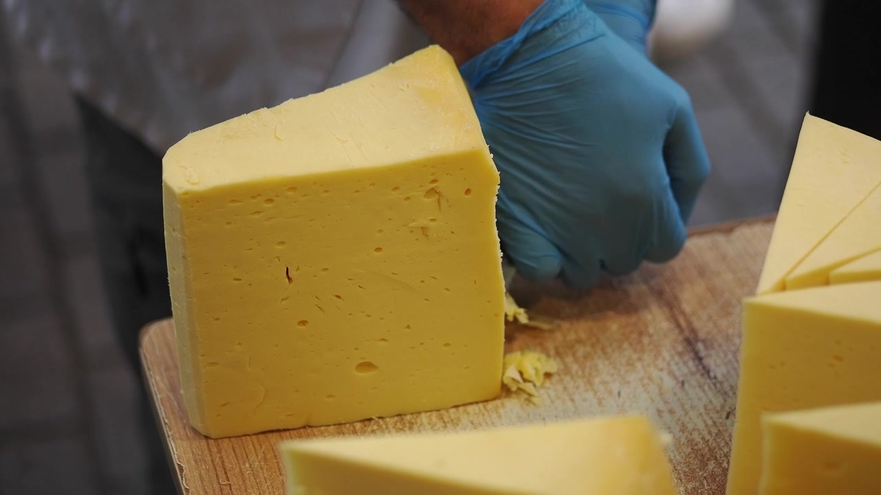 Mano enguantada cortando un gran bloque de queso amarillo