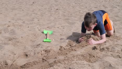 Young-boy-in-a-wetsuit-on-a-beach-digging-in-the-sand