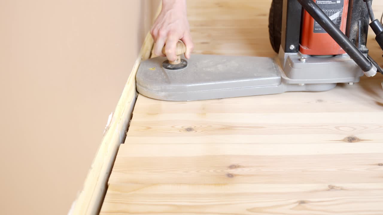 Close-up hand using and assisting electric edge floor sander during wooden floor parquet renovation at home