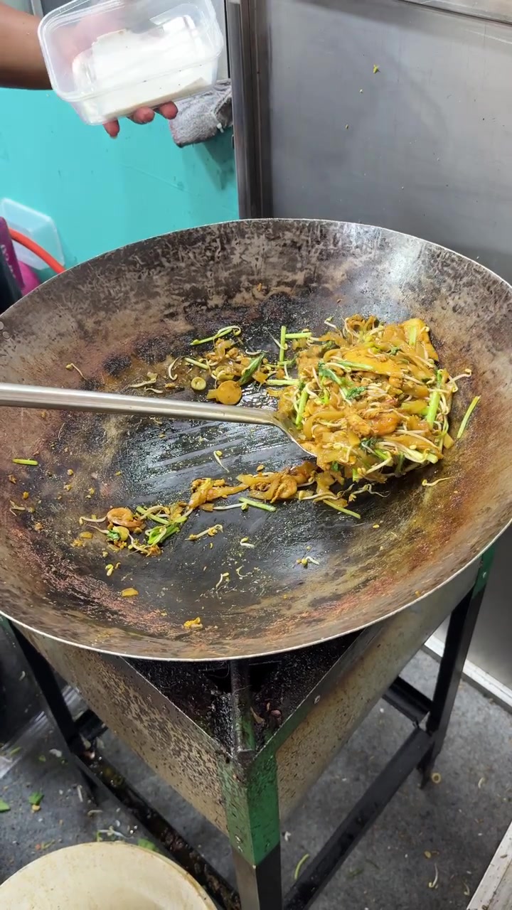 Venditore di street food che salta i noodles in un grande wok