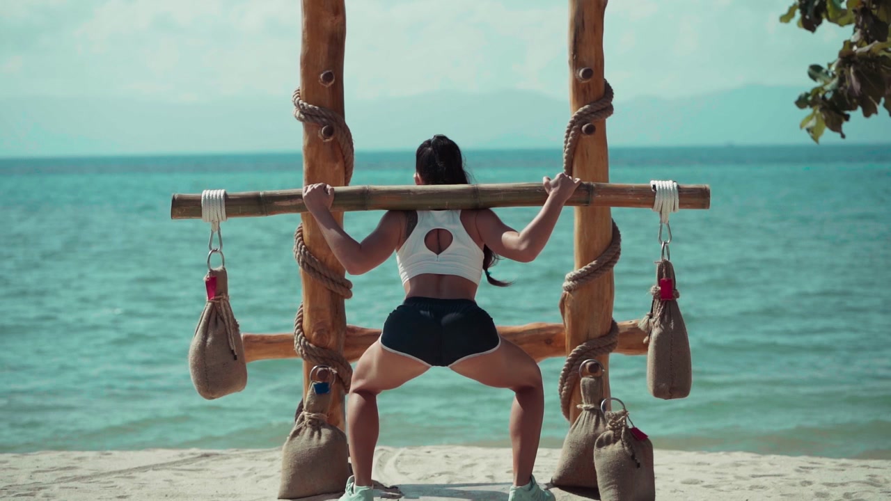 Donna che esegue squat con bilanciere di bambù su una spiaggia tropicale
