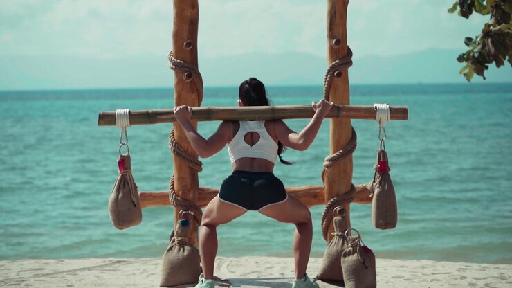 Donna che esegue squat con bilanciere di bambù su una spiaggia tropicale