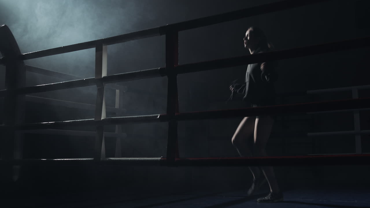 Atleta donna che si allena con la corda in un ring di pugilato fumoso