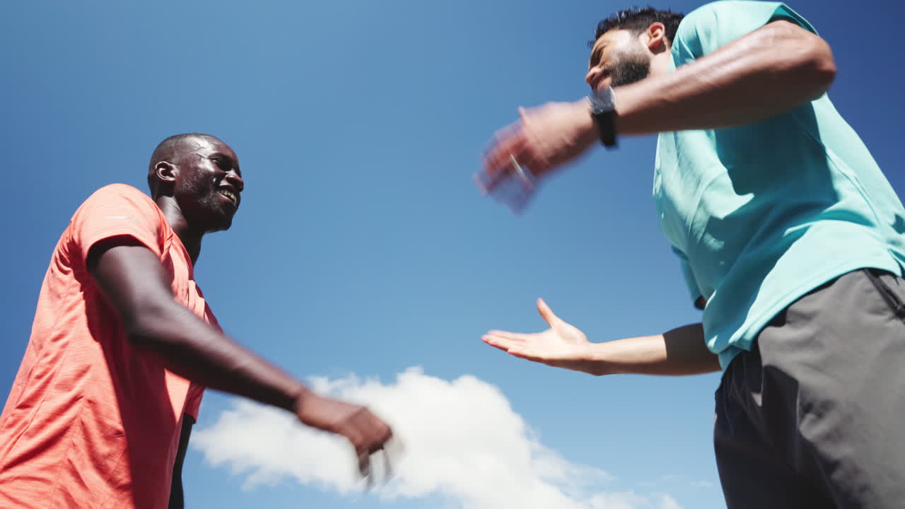 Uomini atletici che si danno il cinque e corrono sotto un cielo blu