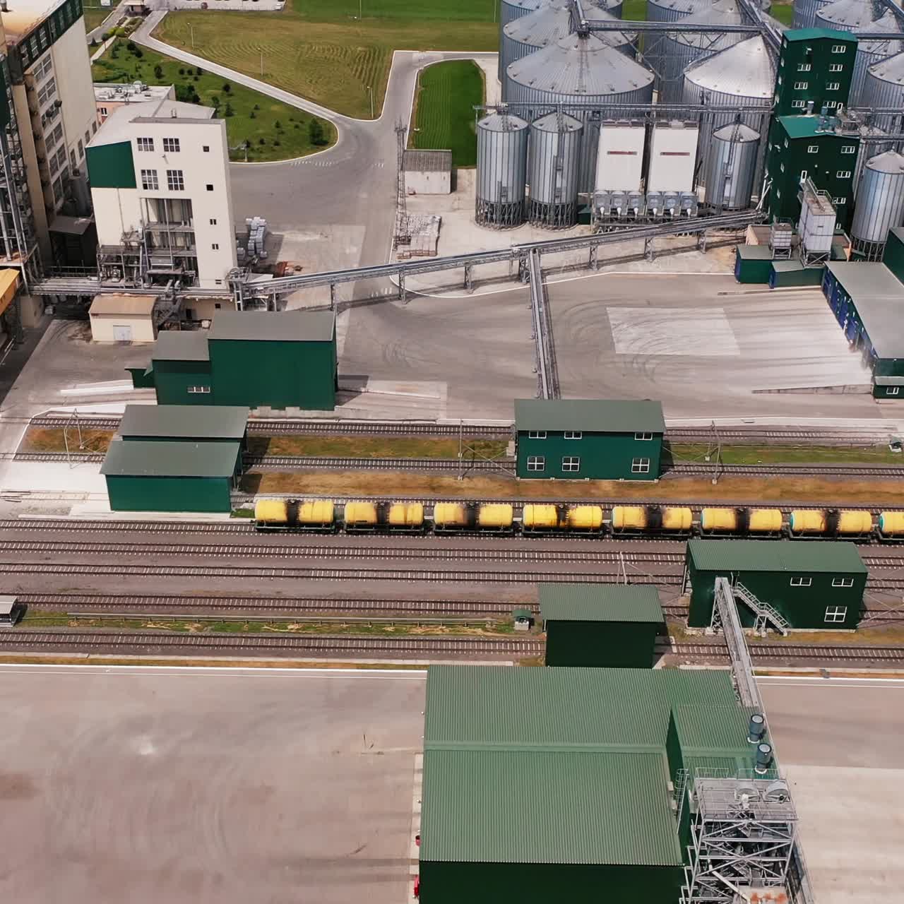 Grain elevators for processing crops. Tremendous metal tanks on the huge plant territory. Thick woods at the backdrop