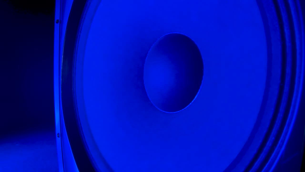 진동하는 베이스 스피커 가까이. 다채로운 네온 클럽 조명에 비추는 검은 스피커는 베이스가 시끄럽을 때 진동합니다. 개념 또는 댄스 파티. 가까이. 느린 모션.