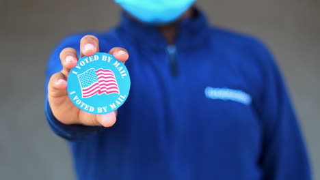 Man-in-mask-from-minority-group-produly-holds-Voted-By-Mail-sticker-during-US-Election-closeup