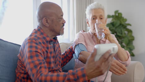 serious senior biracial couple sitting on couch and taking pressure at home, slow motion