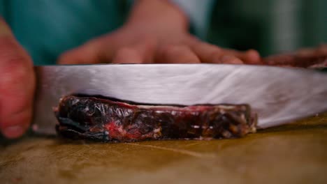 vista de cerca de la mano del chef cortando el bistec con un cuchillo de acero en una tabla de cortar de madera