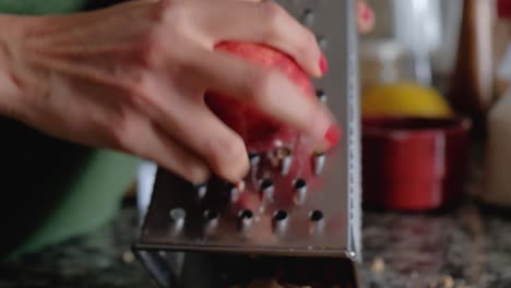 cerca de manos de mujer rallar una manzana roja con piel en un rallador metálico