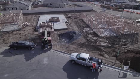 a drone observes an extendable forklift in action, gently lowering the third crate of wood onto a cement foundation within a new neighborhood construction site where no walls have been erected yet