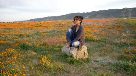 Una-Hermosa-Joven-Llorando-Y-Luciendo-Deprimida-Y-Triste-Sentada-Sola-En-Un-Prado-De-Flores-Silvestres-Con-El-Viento-Soplando-Su-Cabello-Al-Atardecer-En-Cámara-Lenta