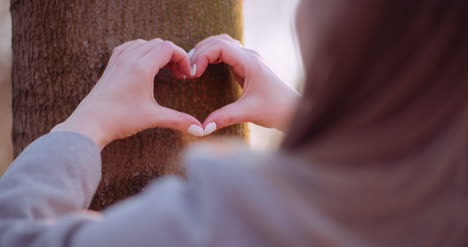 woman make heart shape with hands in forest 1