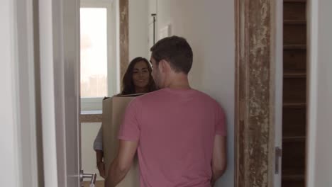 young couple moving to new house, carrying big box together and putting it in living room