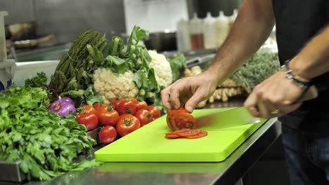 unrecognizable chef slicing red tomato on cutting board in restaurant kitchen