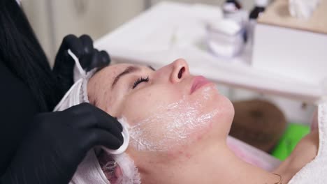 close up view of professional cosmetologist cleaning woman's face using cotton sponge. young woman is lying on the couch during