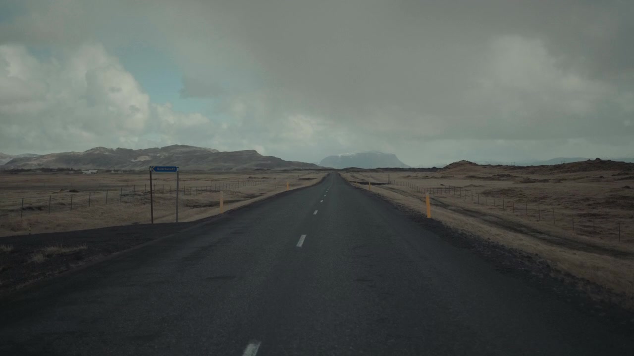 Empty Road Through a Rural Landscape with Mountains Under Cloudy Sky