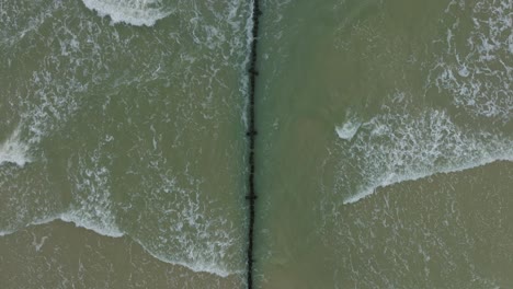 Vista-Aérea-De-Pájaro-De-Un-Viejo-Muelle-De-Madera-En-La-Costa-Del-Mar-Báltico,-Día-De-Invierno-Nublado,-Playa-De-Arena-Blanca,-Postes-De-Madera,-Olas-Golpeando-La-Costa,-Gran-Tiro-De-Drones-Avanzando