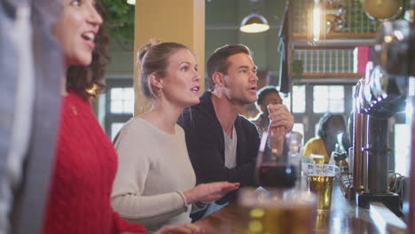 group of excited customers in sports bar watching sporting event on television