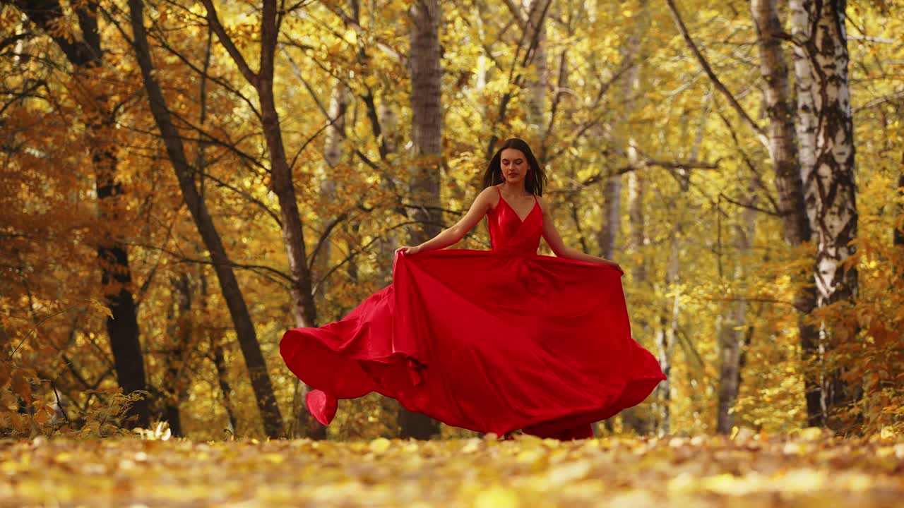 A graceful woman in a flowing red gown dances amid a stunning autumn landscape, surrounded by golden leaves and vibrant trees, radiating beauty and elegance