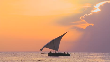 a beautiful shot of a dhow sailboat sailing along the coast of zanzibar against a beautiful sunset