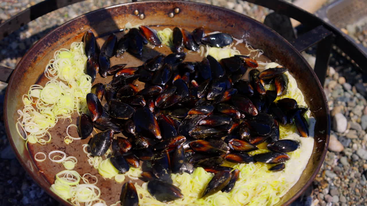Mejillones vertidos en una olla grande y cocinados al aire libre sobre fuego abierto, con vapor ascendente y cocina rústica a la llama. Ideal para vídeo de marisco, cocina culinaria y al aire libre.