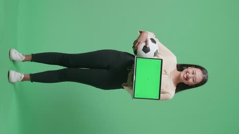 mujer sosteniendo una pelota de fútbol y una computadora portátil con pantalla verde