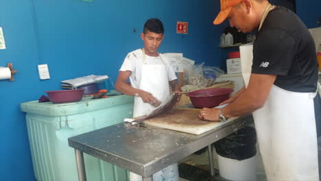 close up of a chef in a restaurant in mexico scaling a freshly caught fish on a cutting board in the kitchen in the back of house