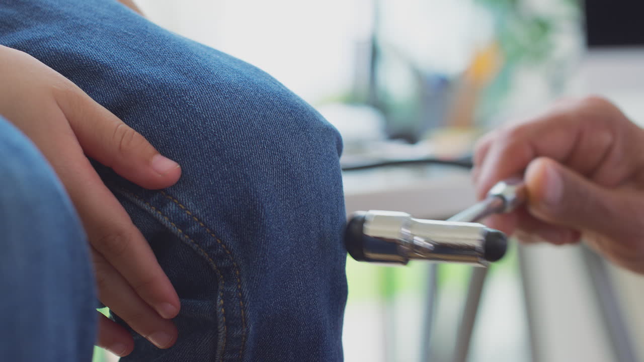 primer plano de un médico o médico de cabecera que lleva una bata blanca examinando a un niño probando sus reflejos con un martillo en la rodilla