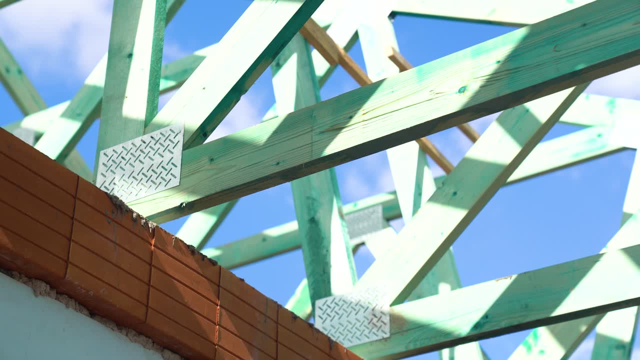 Timber roof trusses above red brick wall under sunny blue sky during framing, closeup