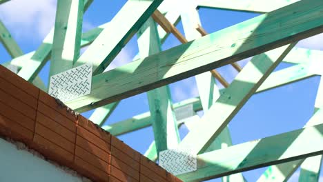 timber roof trusses above red brick wall under sunny blue sky during framing, closeup