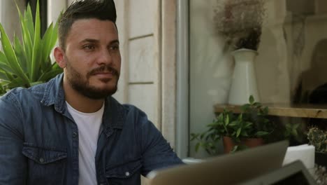 hombre barbudo usando una computadora portátil y hablando con alguien en un café