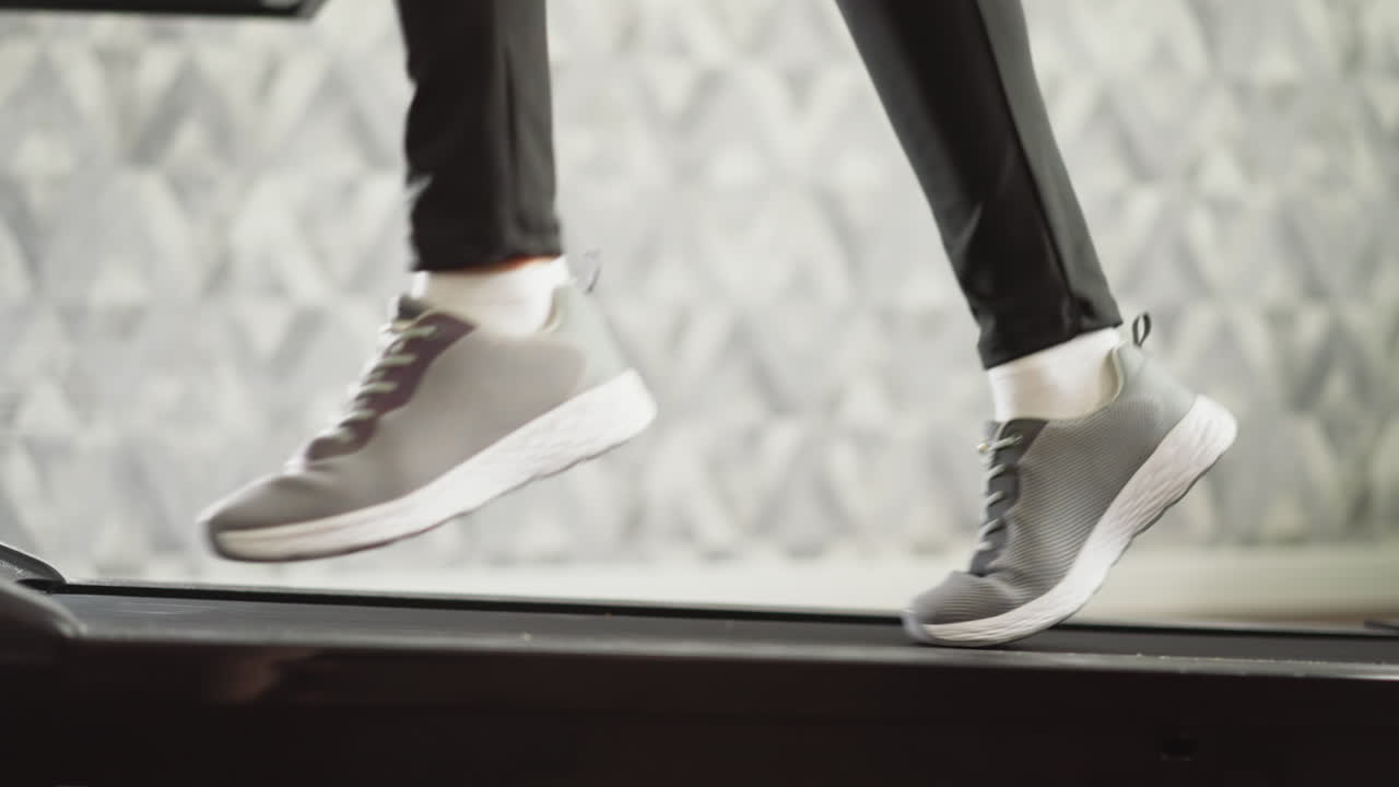 여자 다리는 가정 트레드밀 클로즈업에서 스프린트. 운동 신발을 입은 스포츠 활동 여성은 집에서 운동 기계에서 운동에 참여합니다. 느린 동작