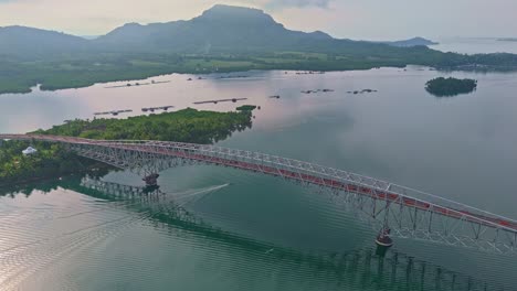 a calm boat glides beneath san juanico bridge in leyte, with mountains in the distance