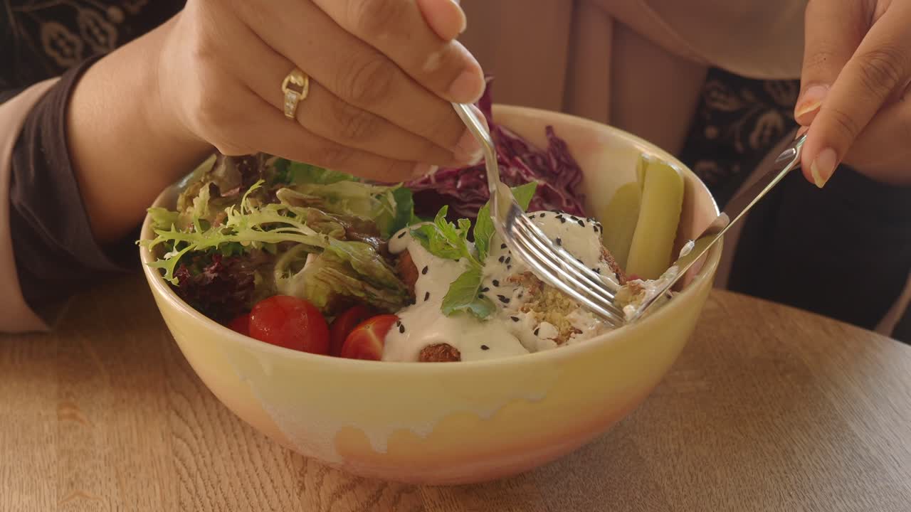 Close-up of a person eating a healthy falafel salad bowl with cutlery