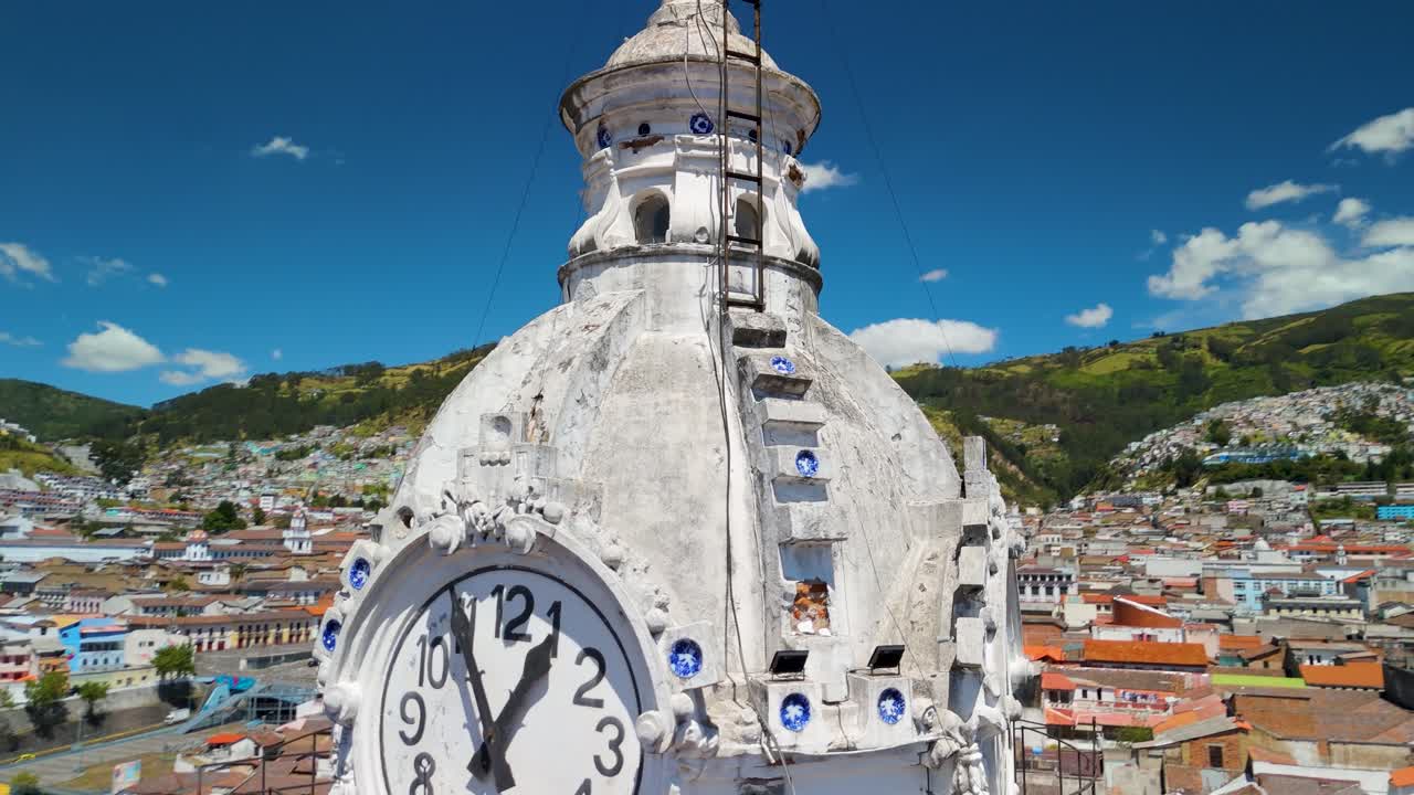 Circoli di parallasse aerea della Basílica Católica Nuestra Señora de La Merced, cupola dell'orologio barocca bianca e usurata con accenti di piastrelle blu, sopra i tetti coloniali di Quito.
