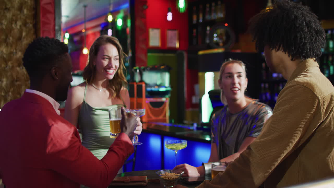 Video of diverse group of happy friends standing at a table drinking and making a toast at a bar
