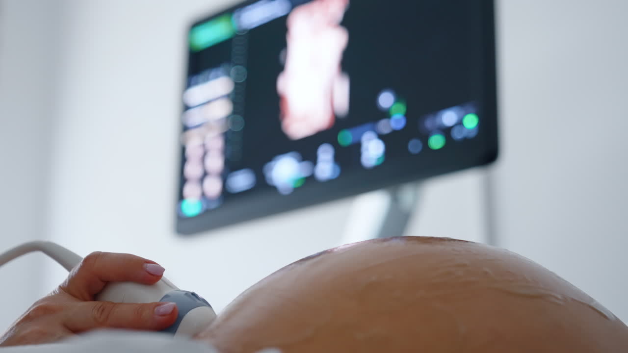 Obstetrician's hand using ultrasound equipment to check the development of a fetal child. Close up. Black screen at backdrop in blur.