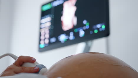 obstetrician's hand using ultrasound equipment to check the development of a fetal child. close up. black screen at backdrop in blur.