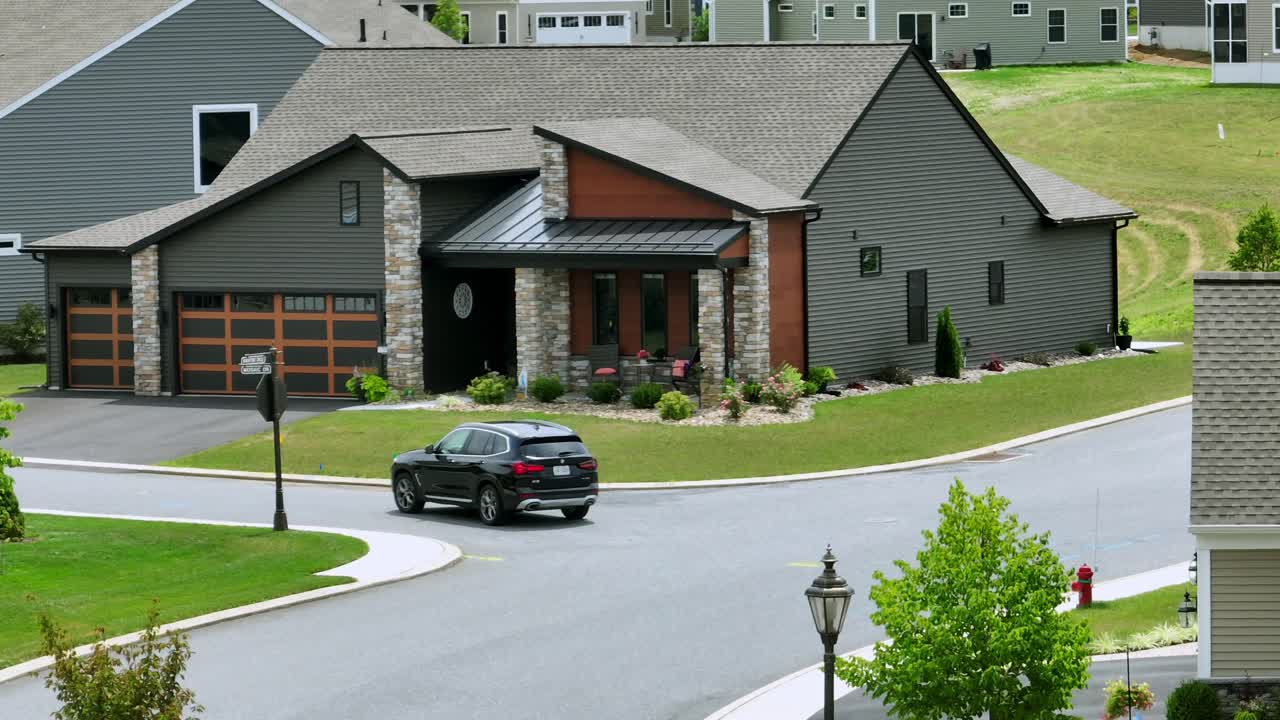 Aerial zoom shot of BMW Car driving on street of american neighborhood. Sunny day in well kept housing area of USA. Tracking shot.