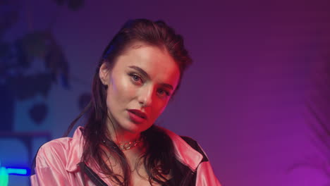 close up of young woman looking at camera in room with neon pink and blue lights