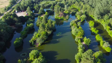 Fishing-Pond-In-Green-English-Rural-Surroundings-In-Norfolk,-UK---aerial-drone-shot